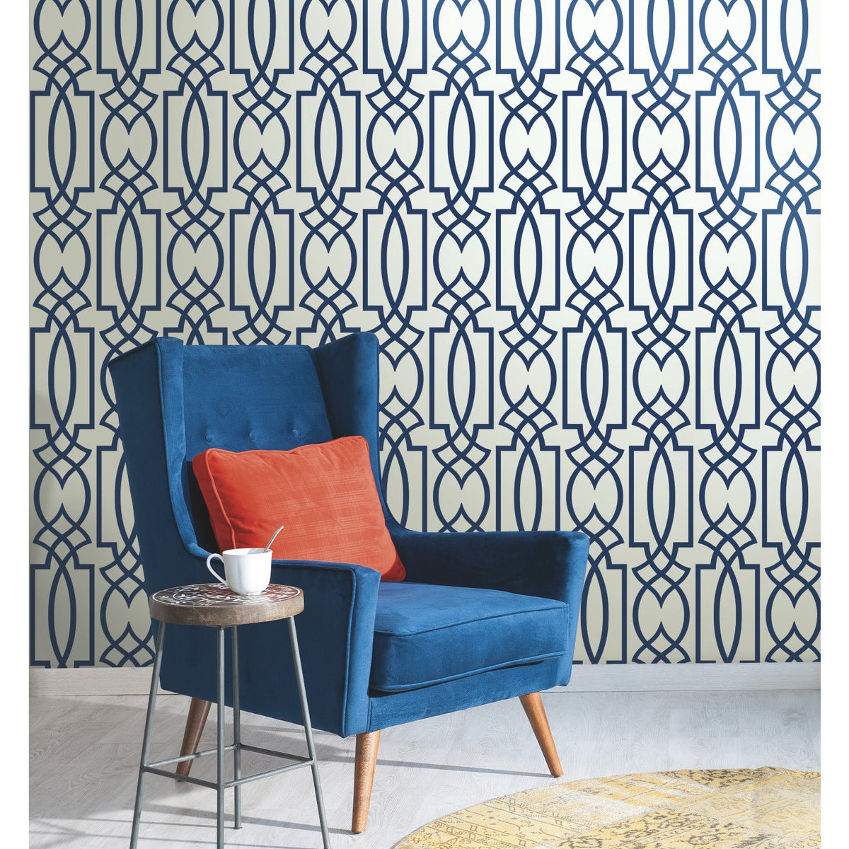 Blue wingback chair with an orange pillow, placed in front of a wall featuring Large Lattice Wallpaper by York Wallcoverings in a dark blue geometric pattern.