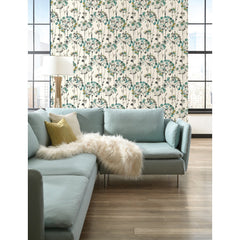 Candice Olson Flourish Wallpaper with a repeating pattern of teal, grey, and brown dandelion-like floral blooms on a cream background, displayed on a wall behind a light blue sectional sofa.