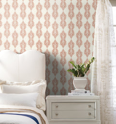A white bed and nightstand are placed beside a potted plant in a bright bedroom, featuring Broadsands Botanica Wallpaper by York Wallcoverings, with cream and pink patterns, and sheer script curtains.