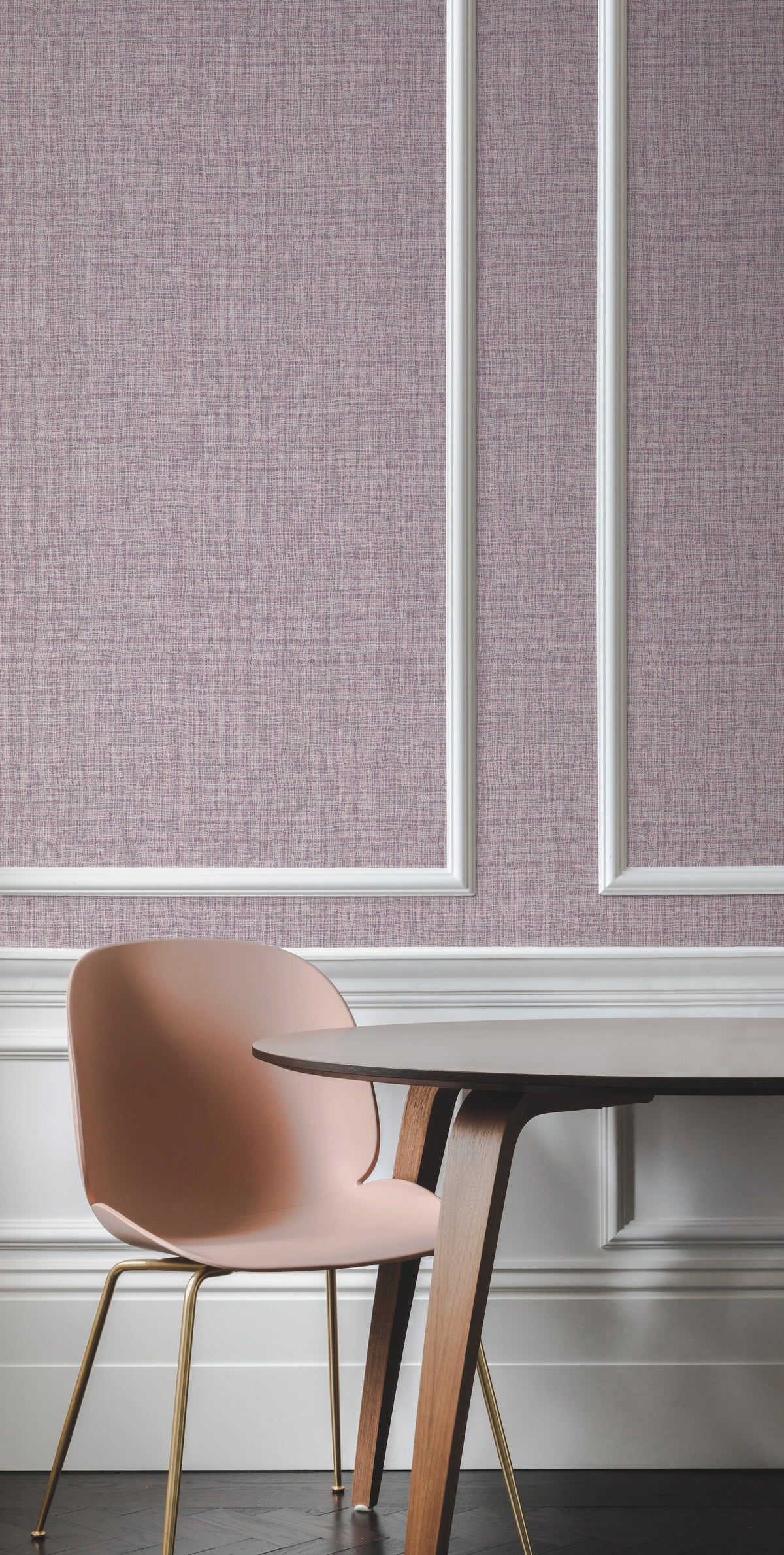 A pink chair and wooden table sit in front of a mauve Caprice Wallpaper by York Wallcoverings, featuring white decorative trim and molding, to create a modern and elegant interior scene.