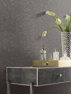 A modern console table with a metallic tray holding glass bottles and a vase of white tulips, set against a textured dark gray Weathered Cypress Wallpaper by York Wallcoverings.