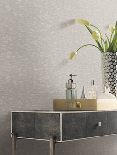A metallic tray with toiletries and a faceted vase holding white tulips sits on a modern, dark-textured console table against a wall adorned with York Wallcoverings’ Weathered Cypress Wallpaper.