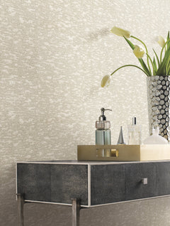 A metallic tray with bottles and a soap dispenser sits on a dark textured console table; a tall silver vase filled with white tulips stands beside it, set against York Wallcoverings’ Weathered Cypress Wallpaper.