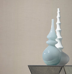 Two modern vases, one glossy light blue with curved shapes and one matte white with stacked segments, stand on a glass surface against a wall adorned with Gossamer Woven Wallpaper by York Wallcoverings.