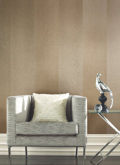Set against a feature wall covered in York Wallcoverings’ Etched Chevron Wallpaper, a modern gray armchair with a textured cushion sits beside a glass table topped with a silver bird sculpture.