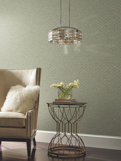 A beige armchair with a fluffy white pillow sits next to a round gold side table holding a small vase of white flowers and books, beneath a modern hanging light, set against Galaxies Wallpaper by York Wallcoverings.