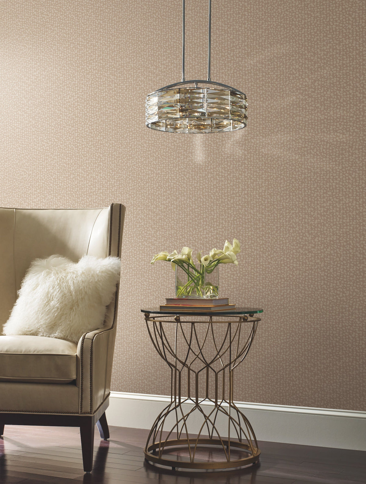 A beige armchair with a white pillow sits beside a round metal side table topped with books and a vase of white flowers, illuminated by a modern glass pendant light, all set against the Galaxies Wallpaper by York Wallcoverings.
