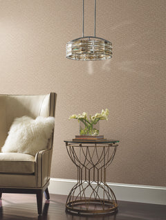 A beige armchair with a white pillow sits beside a round metal side table topped with books and a vase of white flowers, illuminated by a modern glass pendant light, all set against the Galaxies Wallpaper by York Wallcoverings.