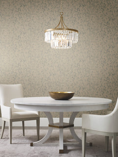 A round white table with two white chairs, a gold bowl centerpiece, and a crystal chandelier above, set against Luminous Branches Wallpaper by York Wallcoverings.