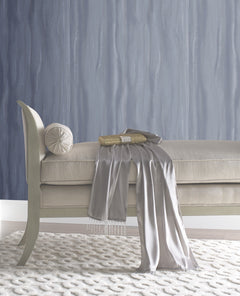 A beige upholstered bench with a round bolster cushion, a gold clutch, and a draped silver scarf, set against Candice Olson Fantasy Faux Bois Wallpaper by York Wallcoverings.