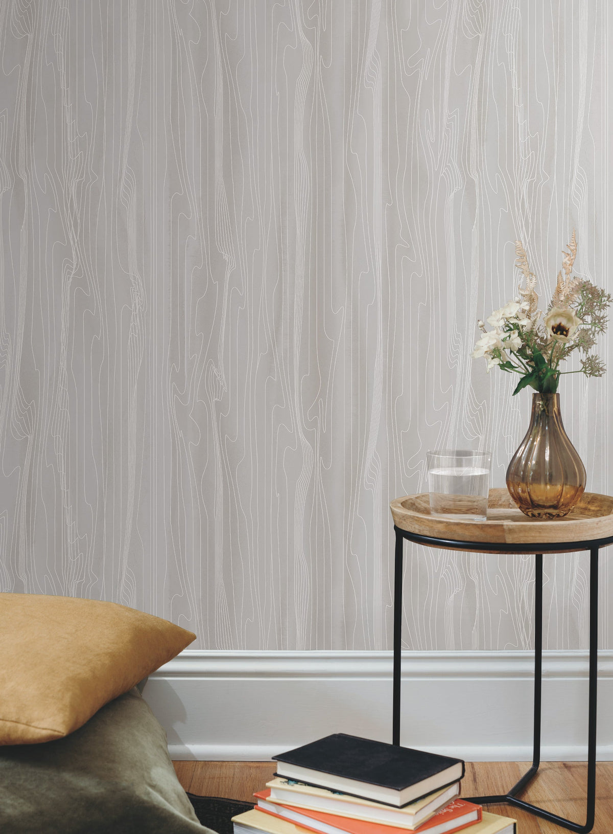 Candice Olson Fantasy Faux Bois Wallpaper in light gray with a linear wood grain pattern displayed behind a side table with a glass of water and a floral arrangement.