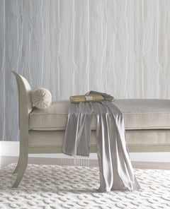 An upholstered bench with a small bolster pillow, a gold clutch, and a draped gray scarf, set against York Wallcoverings Candice Olson Fantasy Faux Bois Wallpaper featuring a white wood-grain pattern.