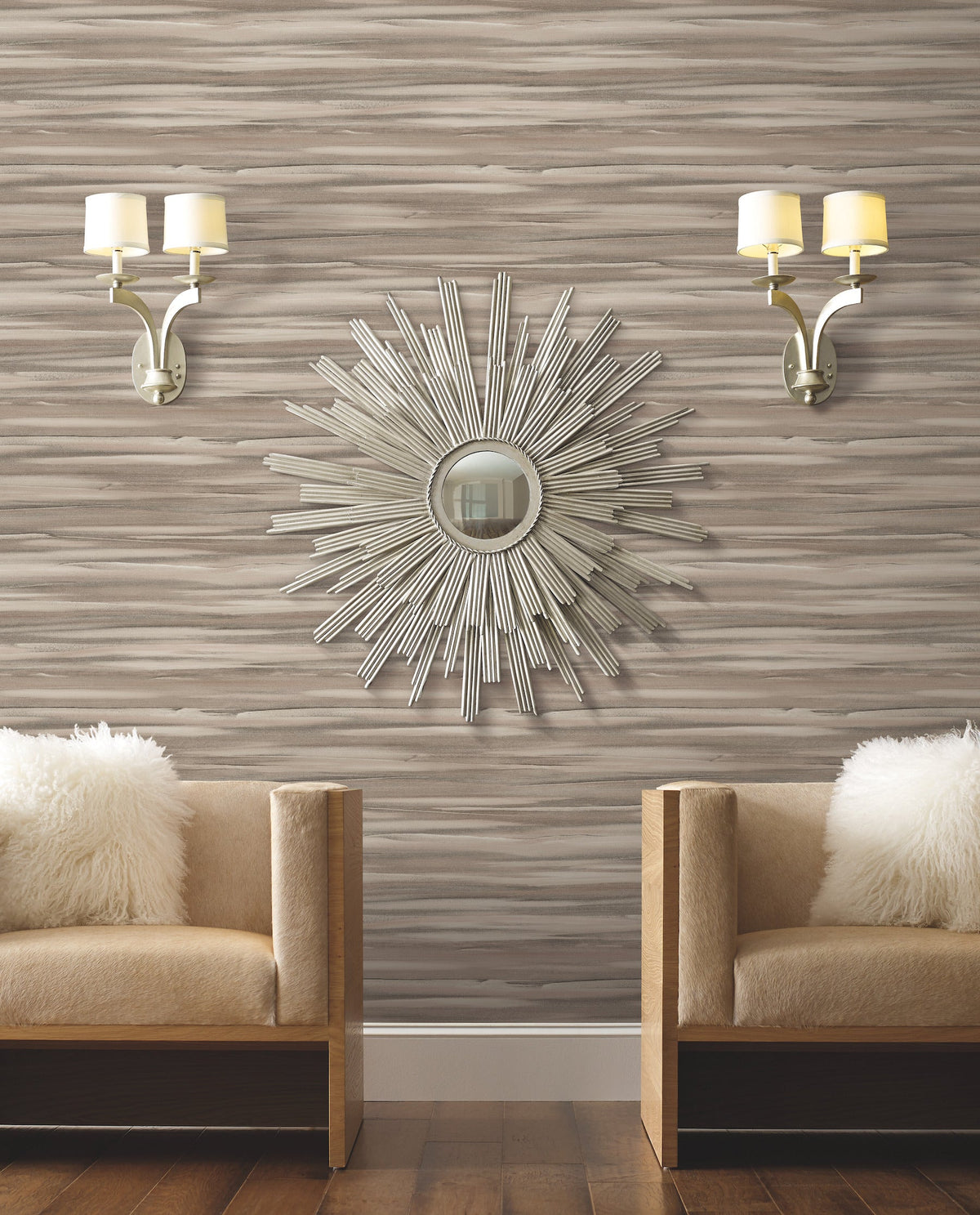Two armchairs with fuzzy white pillows sit against a wall covered in Candice Olson Sanctuary Wallpaper, accented by a sunburst mirror and two wall sconces.