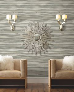 Candice Olson Sanctuary Wallpaper featuring a horizontal, brushstroke-style pattern in shades of gray, white, and blue, displayed behind two tan chairs and a sunburst mirror.