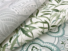 Three overlapping sheets of York Wallcoverings’ Willow Grove Wallpaper: one featuring gray leaf patterns, one showcasing green leafy vines, and one displaying blue and white ornate designs.