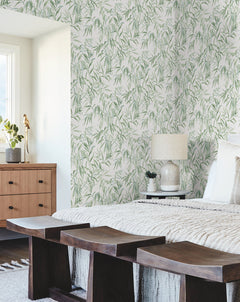 Bedroom featuring Willow Grove Wallpaper by York Wallcoverings, a wooden bed adorned with pillows and a lamp, and dark benches. A dresser with decor sits beside a window that fills the space with natural light, creating a cozy and modern atmosphere.