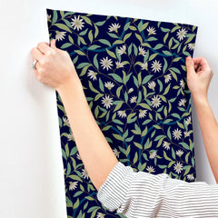 A person in a striped shirt presses York Wallcoverings’ Jasmine Wallpaper onto a white wall, adjusting it with both hands.