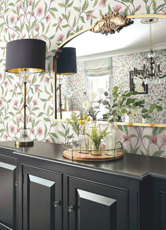 Jasmine Wallpaper by York Wallcoverings, a black lamp, a gold-trimmed mirror, and glass vases with greenery sit atop a black sideboard, creating a stylish and elegant interior.