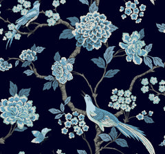 Fanciful Wallpaper by York Wallcoverings features a seamless pattern of blue and white birds perched on blossoming branches with flowers and leaves, set against a dark background. A butterfly flutters near the lower left corner.