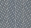 The Ronald Redding Atelier Herringbone Wallpaper by York Wallcoverings features a gray concrete surface accented with white diagonal lines in a repeating chevron pattern, creating a geometric and modern design.