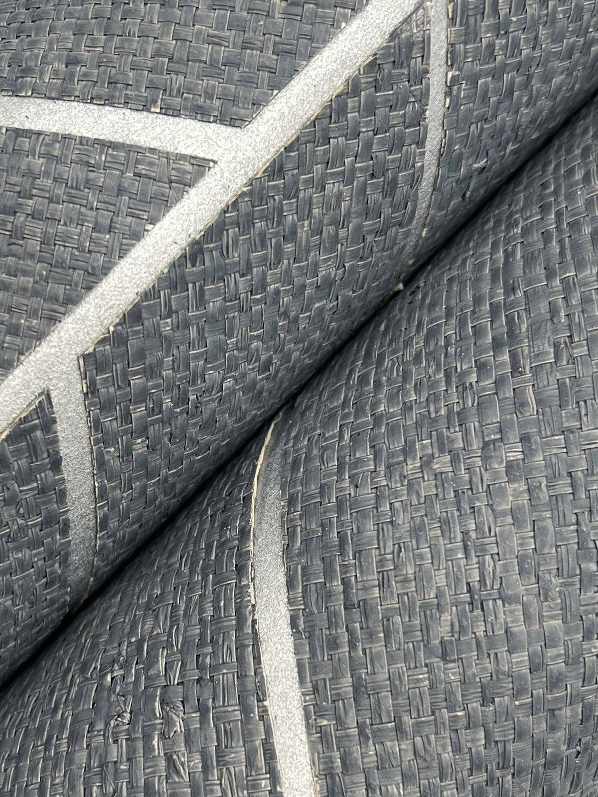 Close-up of two rolls of Ronald Redding Atelier Herringbone Wallpaper by York Wallcoverings, featuring a textured gray surface with a woven pattern and thin, shiny, light-colored diagonal lines.