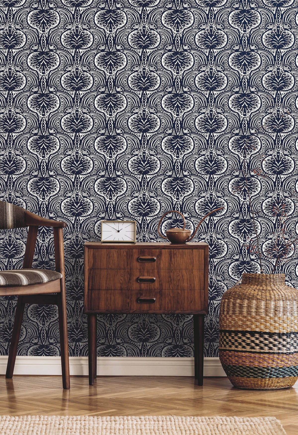 Ronald Redding Lotus Palm Wallpaper featuring a repeating dark blue and white stylized floral pattern behind a wooden nightstand, a chair, and a woven basket.