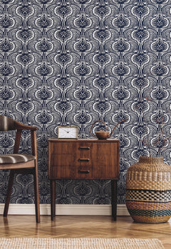 Ronald Redding Lotus Palm Wallpaper featuring a repeating dark blue and white stylized floral pattern behind a wooden nightstand, a chair, and a woven basket.