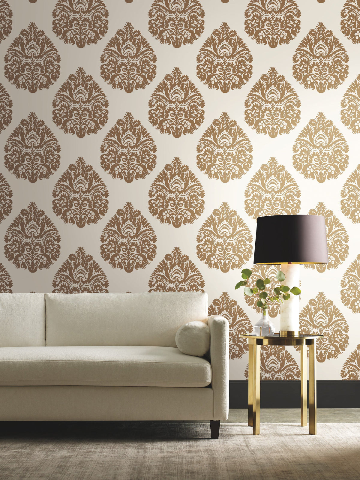 Off-white sofa and gold side table with a lamp against a wall covered in brown and white Ronald Redding Teardrop Damask Wallpaper.