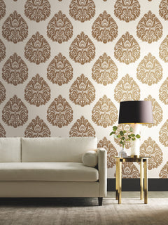 Off-white sofa and gold side table with a lamp against a wall covered in brown and white Ronald Redding Teardrop Damask Wallpaper.