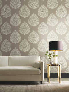 Ronald Redding Teardrop Damask Wallpaper in beige with a repeating white teardrop-shaped pattern, displayed behind a white sofa and a side table with a lamp.