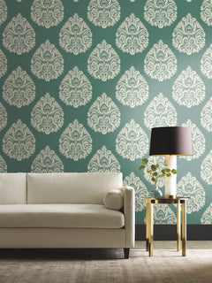 Ronald Redding Teardrop Damask Wallpaper featuring a repeating white teardrop-shaped pattern on a dark green background, displayed behind a white sofa and a side table with a lamp.