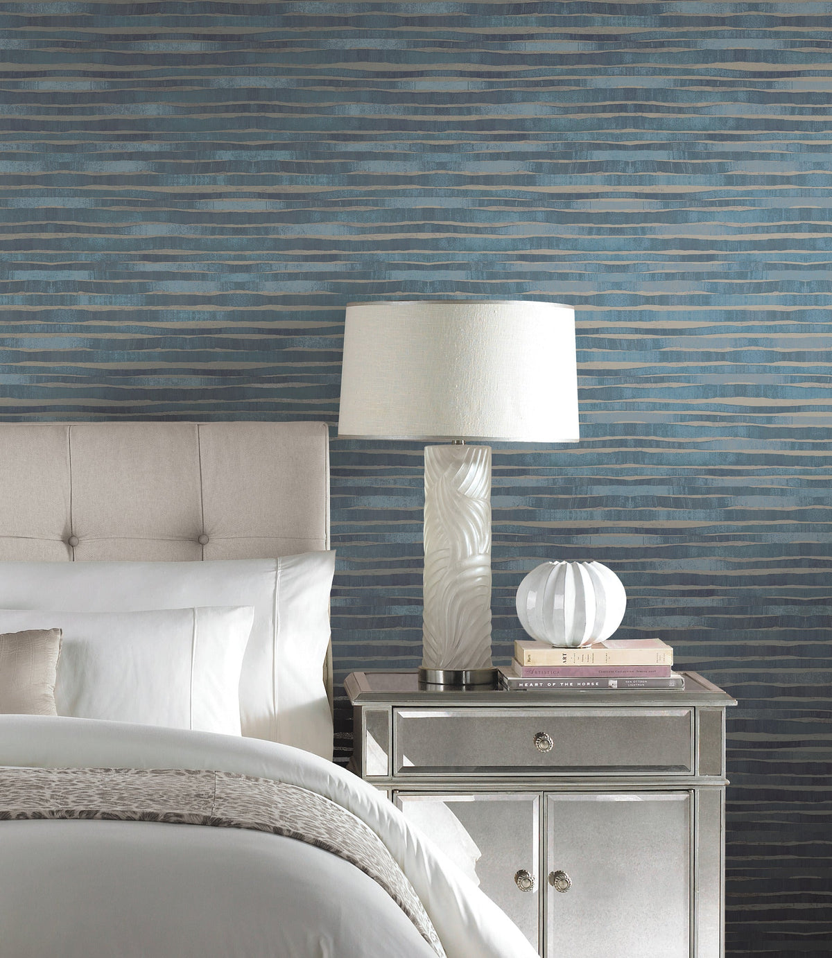 Ronald Redding Dreamscapes Wallpaper featuring horizontal, wavy bands of blue and gray behind a bedroom nightstand and lamp.