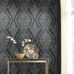 Ronald Redding Charleston Damask Wallpaper in grey and blue sits behind a glass console table holding a decorative plate and an orchid.