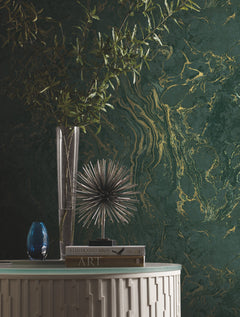 Ronald Redding Polished Marble Wallpaper in dark green with gold veining, displayed behind a glass vase with branches, a spiky metal sculpture, and two books on a white console table.