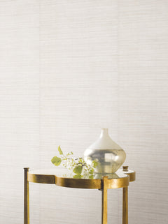 A glass vase and a flowering branch rest on a small metal table against a textured, light-colored Ronald Redding Silk Elegance Wallpaper.