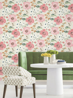 A green tufted bench and a white patterned chair surround a small white round table with yellow flowers, set against York Wallcoverings’ Evelyn Floral Wallpaper.