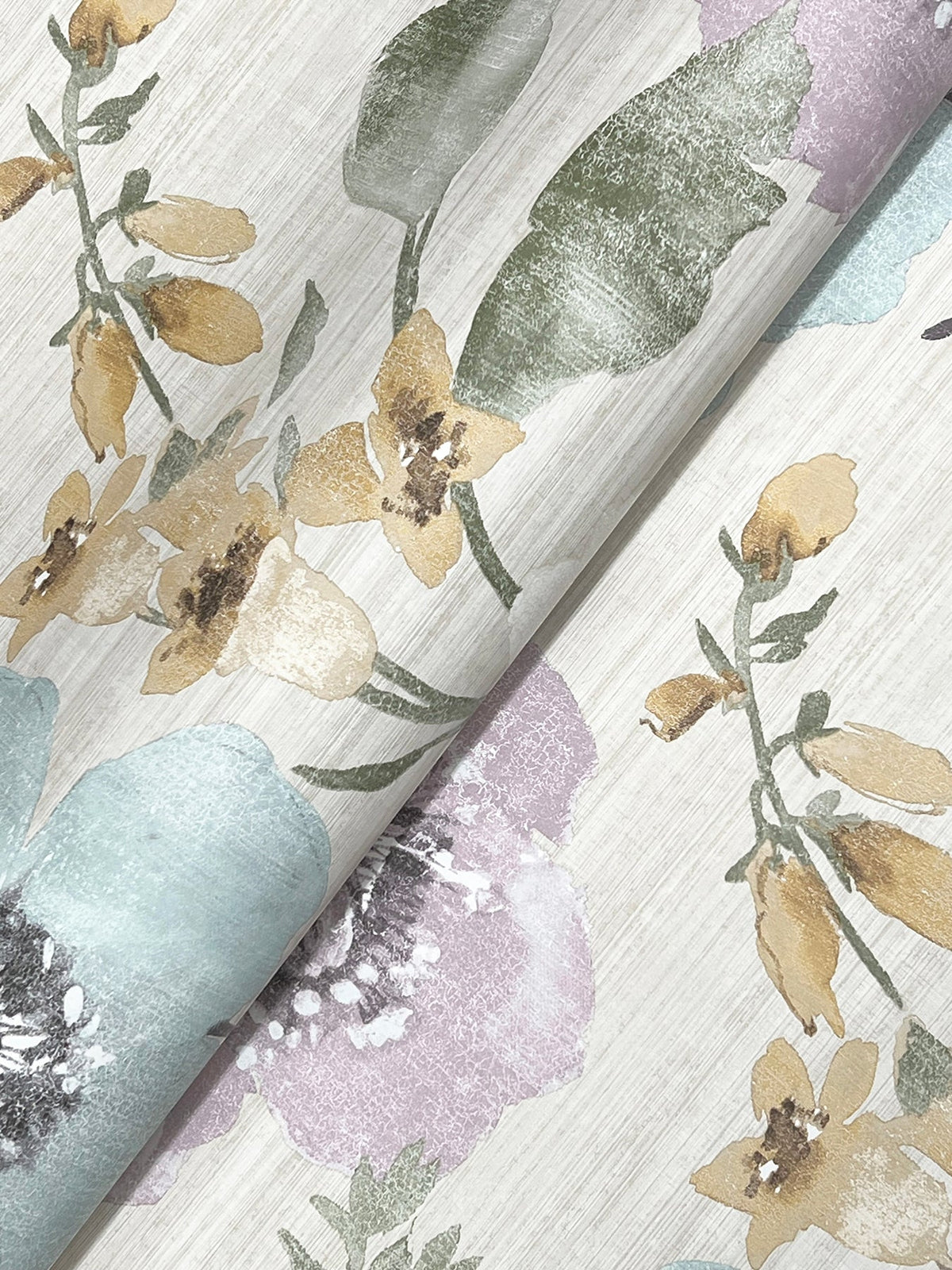 York Wallcoverings’ Evelyn Floral Wallpaper features a repeating botanical design with yellow, green, and purple flowers and leaves set against a light, textured background. The wallpaper is shown folded to highlight its elegant floral pattern.