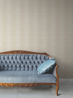 A vintage wooden sofa with blue tufted upholstery and a blue cushion with tassels is set against Colbert Stripe Textured Wallpaper and a white tiled floor.