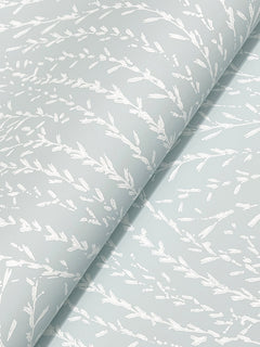 Close-up of Willow Song Botanical Wallpaper by York Wallcoverings, featuring a delicate white botanical pattern of leafy branches on a light blue background. The wallpaper is slightly folded, highlighting its repeating nature-inspired design.