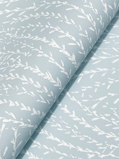 Willow Song Botanical Wallpaper by York Wallcoverings features a light blue background adorned with a delicate white leafy branch pattern. The wallpaper has a subtly glossy finish and, when applied, can display gentle diagonal folds that enhance its soft botanical design.