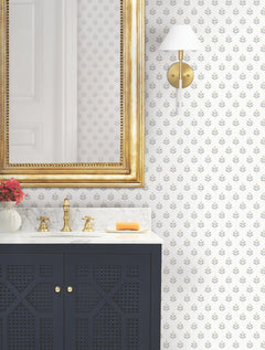 A bathroom featuring a gold-framed mirror, gold faucet, marble countertop, black vanity, a small bouquet of flowers, a bar of soap, a gold and white wall sconce, and Serene Villa Floral Stamp Wallpaper by York Wallcoverings.
