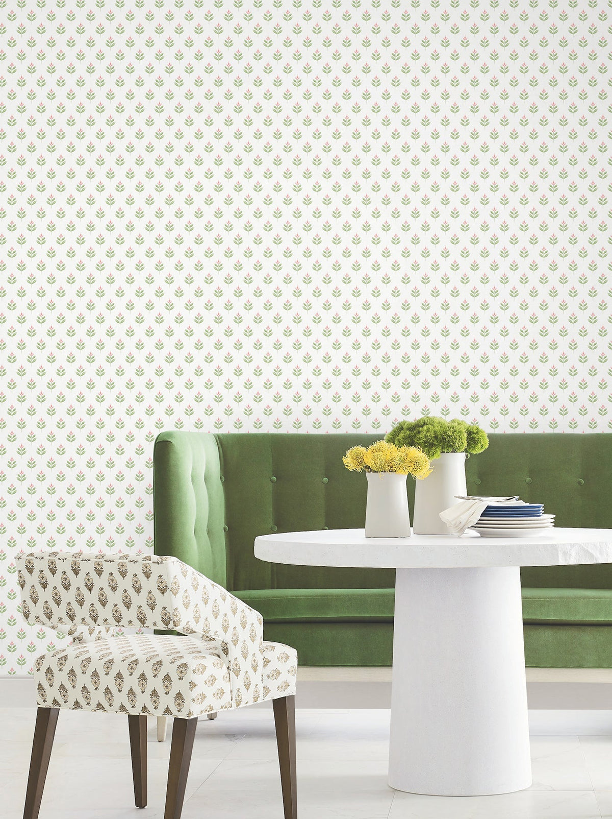 A green velvet sofa, a white round table adorned with yellow flowers, and a patterned chair are arranged in a room featuring Serene Villa Floral Stamp Wallpaper by York Wallcoverings. The modern decor creates a soft, elegant atmosphere.