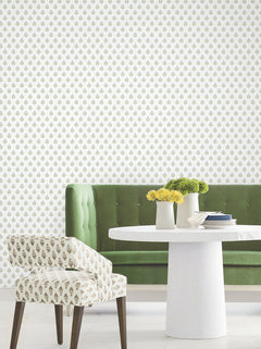 A green velvet banquette, white round table topped with yellow flowers in vases, and a patterned accent chair are featured in a modern, bright room with Serene Villa Floral Stamp Wallpaper by York Wallcoverings, showcasing a small green and yellow floral motif.