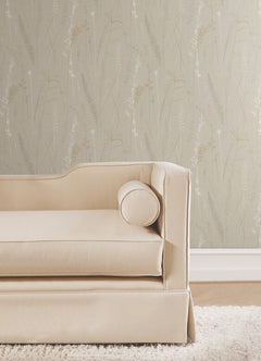 A beige upholstered sofa with a round bolster pillow sits on a white shag rug in front of Meadow Splendor Botanical Wallpaper in light gray.