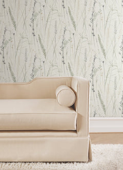 A light beige sofa with a round cushion sits in front of a wall covered in Meadow Splendor Botanical Wallpaper featuring a delicate grass pattern.
