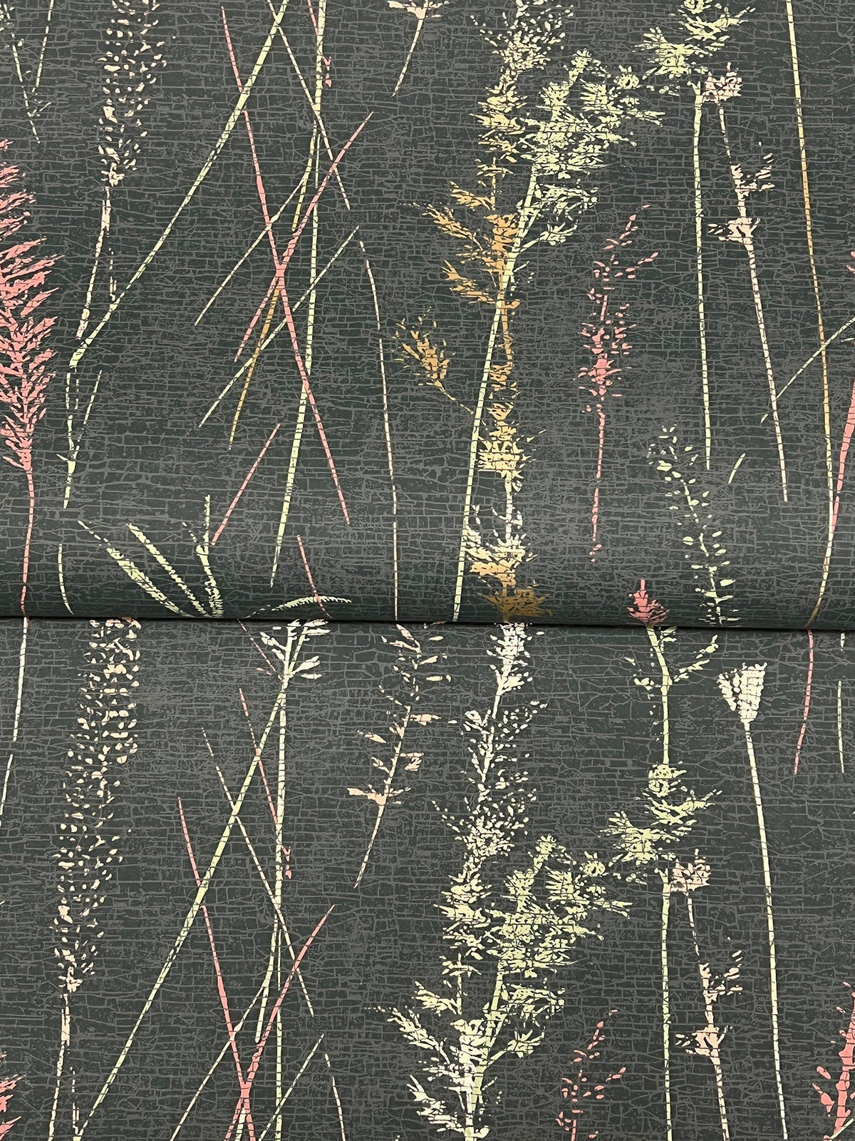 The Meadow Splendor Botanical Wallpaper showcases a dark background adorned with tall, delicate grasses in subtle shades of pink, yellow, and green for a natural, botanical effect. A horizontal seam is visible across the center.