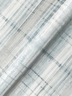 A close-up of Vanishing Point Striated Wallpaper by York Wallcoverings, featuring textured white, gray, and soft blue tones with a subtle, abstract linear pattern and a gentle sheen. The wallpaper is partially rolled to highlight its texture and print.