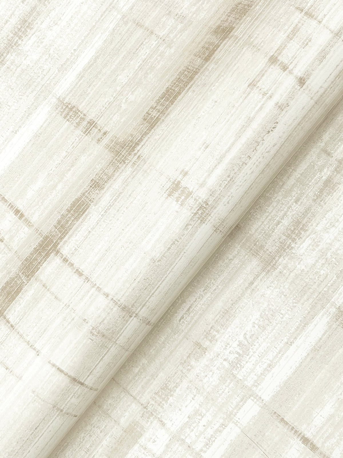 A close-up of York Wallcoverings’ Vanishing Point Striated Wallpaper shows its cream-colored surface, detailed with subtle beige and taupe horizontal and vertical lines that form a soft, abstract plaid pattern. The wallpaper is rolled at a diagonal angle.