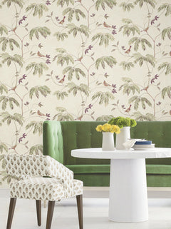 A green tufted sofa, a round white table with yellow and green flowers, and a patterned chair sit in front of York Wallcoverings’ Cillian Botanical Bird Trail Wallpaper.