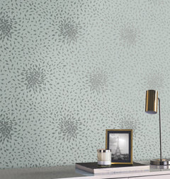 A desk with a gold lamp, a framed Eiffel Tower photo, a candle, and a book sits in front of a light blue wall adorned with York Wallcoverings’ Petite Leaves Wallpaper.